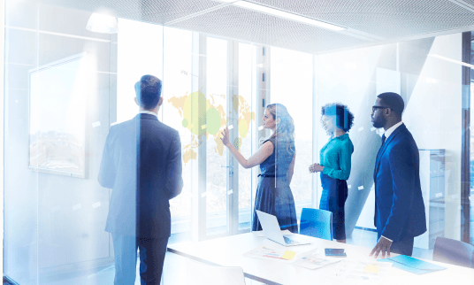 A group of 4 business professionals discussing notes in an office meeting room.